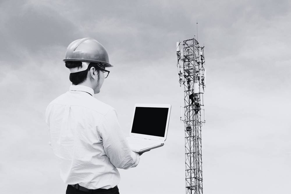 Engineer with a laptop beside a telecom tower